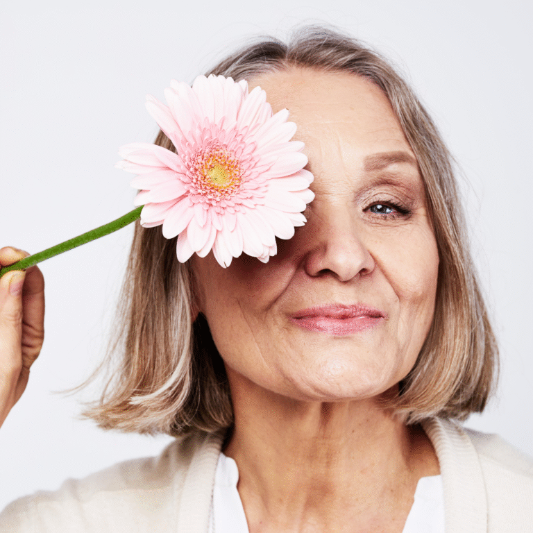 A woman holding a pink gerbera flower over one eye.