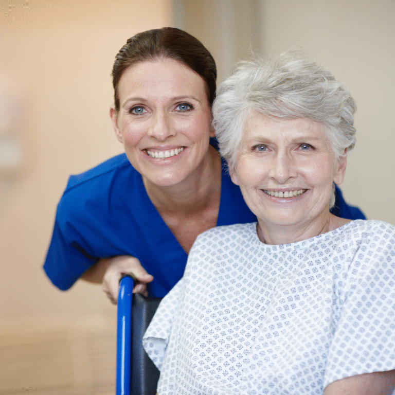 A caregiver in blue scrubs beside an older woman seated in a wheelchair.