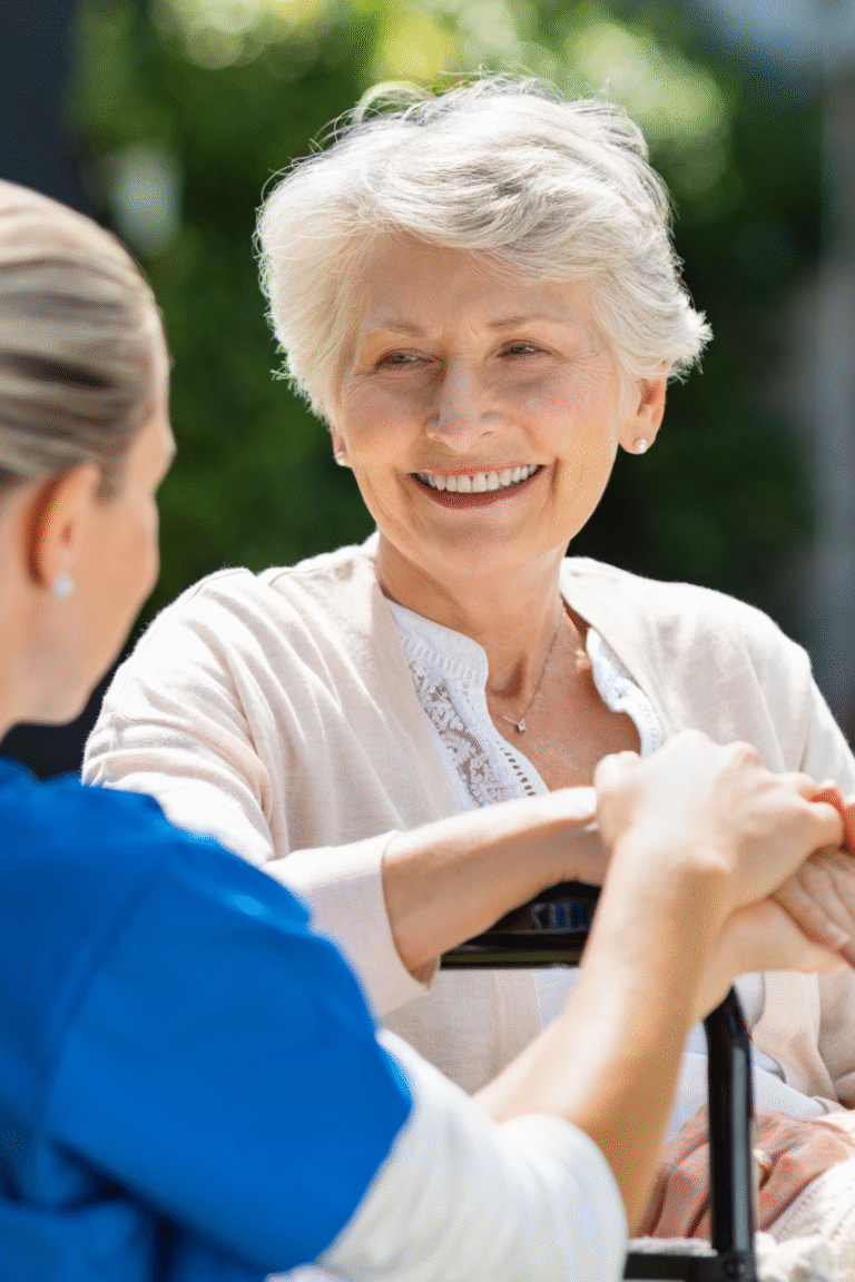 An older woman smiling during a conversation with a caregiver outdoors.