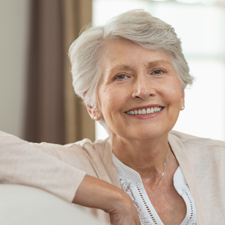 An older woman smiling while seated at home.