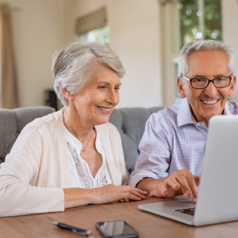 An older couple smiling while using a laptop at home.