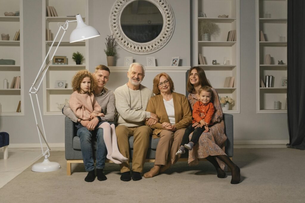 A multi-generational family sitting together on a sofa in a warm living room.