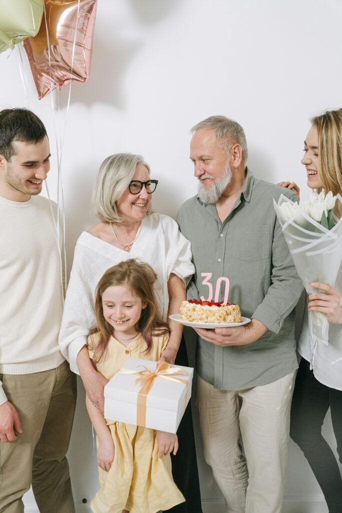 A multigenerational family gathers indoors to celebrate a birthday with cake and gifts.