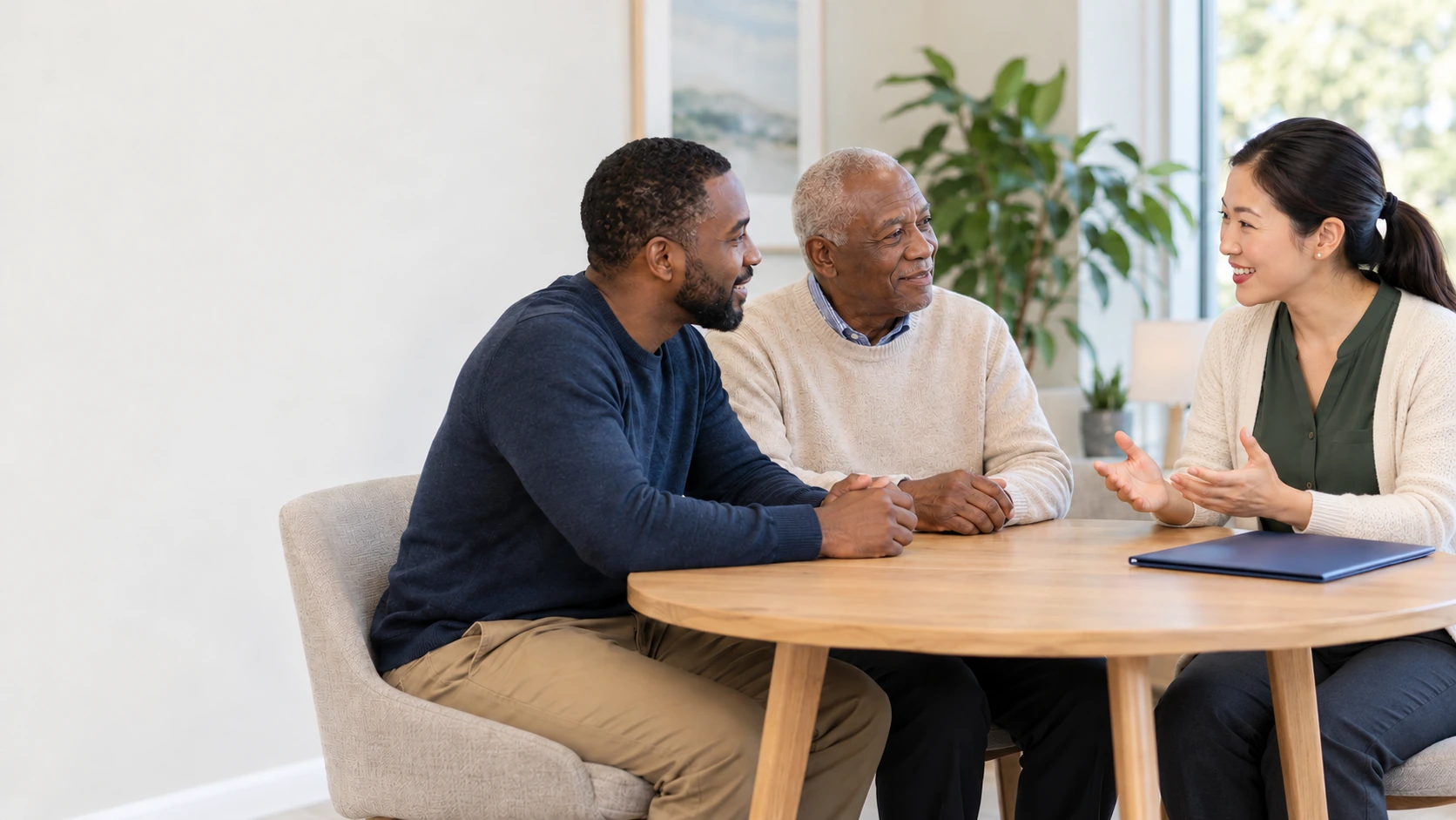 An older father and son discuss care with an advisor in an ivory cardigan.