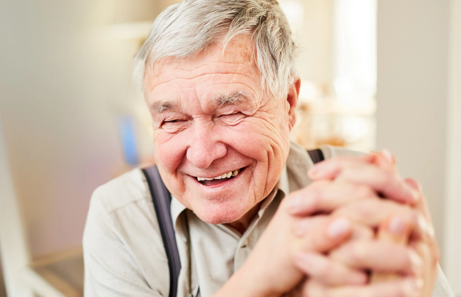 An older man smiles with his hands clasped in front of him. BestCareMatch editorial photo.